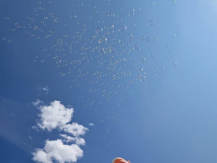 Baloane de săpun, cer albastru, jucarie în mâna pentru copii, distractie în aer liber.